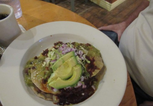 A plate of enchiladas topped with avocado, guacamole, lettuce, and onions, served with a side of beans.
