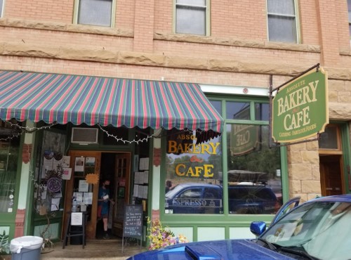 A quaint bakery café with a striped awning, large windows, and a sign reading "Absolute Bakery Café."