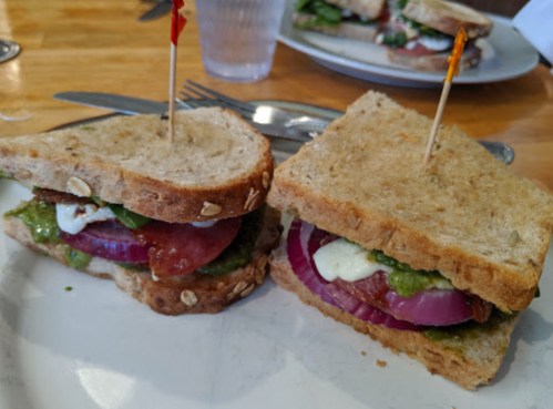 A sandwich with layers of tomato, onion, lettuce, and sauce, served on whole grain bread with toothpicks.