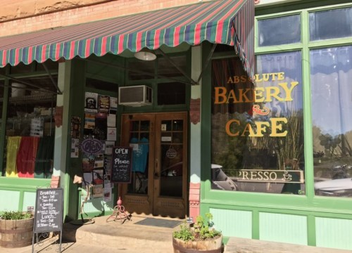 A charming bakery and café with a colorful awning, open sign, and decorative storefront in a historic building.