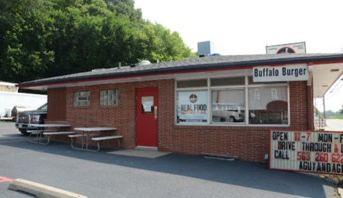 A small brick building with a red door and sign for "Buffalo Burger," featuring outdoor seating and a parking area.