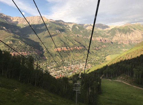 A scenic view from a ski lift, overlooking a valley with mountains and a small town below.