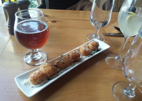 A plate of crispy appetizers on a wooden table, accompanied by glasses of beer and water.