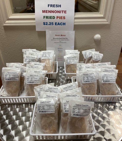 Baskets of fresh Mennonite fried pies, labeled with flavors and prices, displayed on a shiny surface.