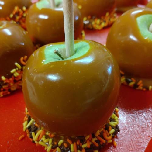 Close-up of caramel apples on a red surface, coated with colorful sprinkles and wooden sticks for easy handling.