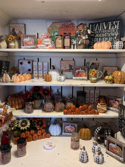A cozy display of fall decorations, including pumpkins, candles, and signs, arranged on wooden shelves.