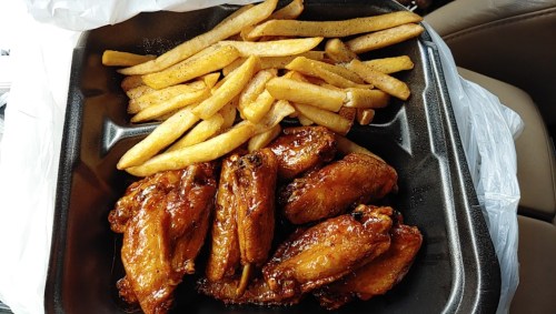 A takeout container with crispy chicken wings glazed in sauce and a side of golden French fries.