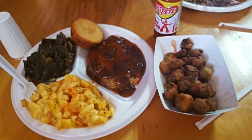 A plate of Southern food featuring collard greens, macaroni and cheese, cornbread, meatloaf with sauce, and fried okra.