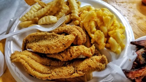A plate of fried catfish fillets, crinkle-cut fries, and macaroni and cheese.