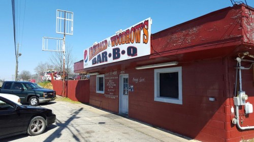 A red building with a large sign reading "Woodrow's Bar-B-Q" and parked cars outside on a sunny day.