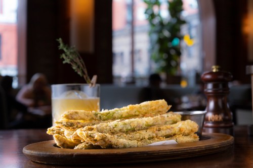 A plate of crispy fried green beans next to a cocktail in a cozy restaurant setting.