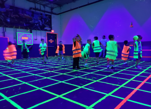 Children in neon vests play in a dark room with glowing grid lines and vibrant colors.