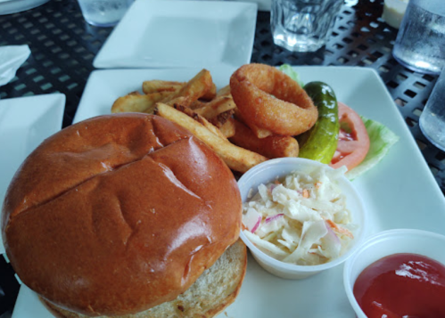 A plate with a burger, fries, onion rings, a pickle, tomato, lettuce, coleslaw, and ketchup.