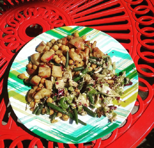 A colorful plate of sautéed vegetables and chickpeas on a vibrant red table.