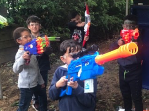 A group of children play with colorful toy guns in a wooded area, smiling and posing for the camera.