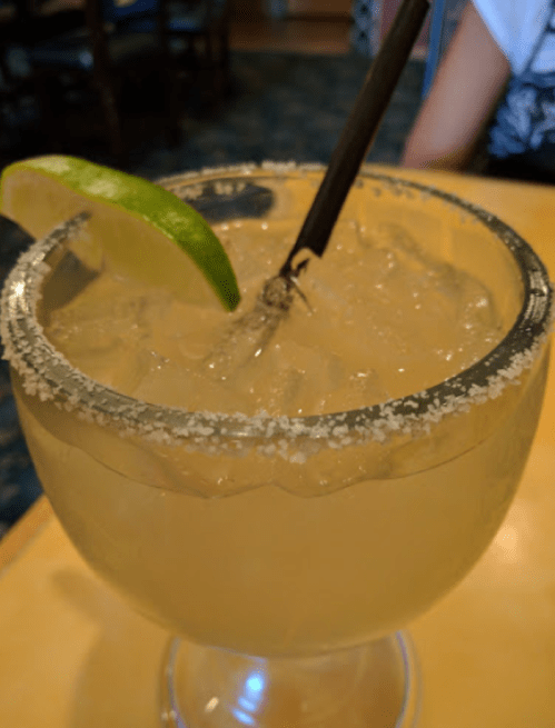 A close-up of a margarita in a glass with a salted rim, garnished with a lime wedge and a straw.