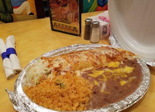 A plate of enchiladas with rice, refried beans, and shredded lettuce, served in a restaurant setting.