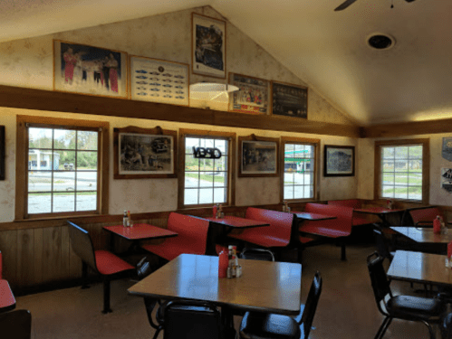 Interior of a diner with red chairs, wooden walls, and framed photos on the walls, featuring large windows.