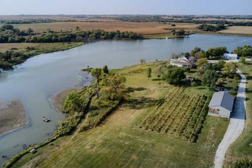 Aerial view of a serene landscape featuring a river, fields, and a house surrounded by trees and greenery.