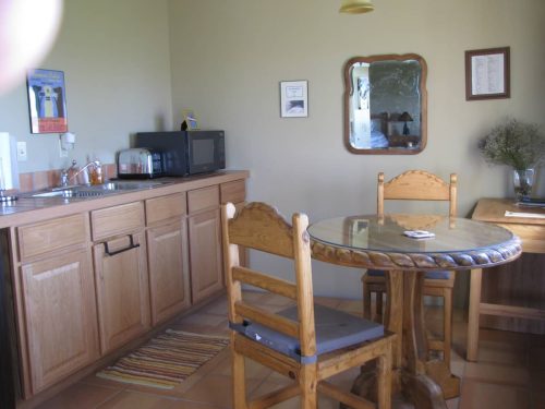 A cozy kitchen with wooden cabinets, a round table, two chairs, a microwave, and a mirror on the wall.