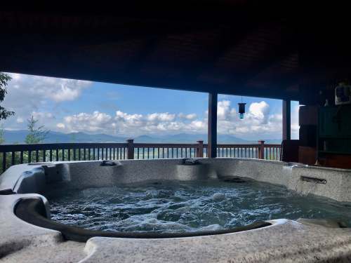 A hot tub with bubbling water, overlooking a scenic view of mountains and clouds from a wooden deck.