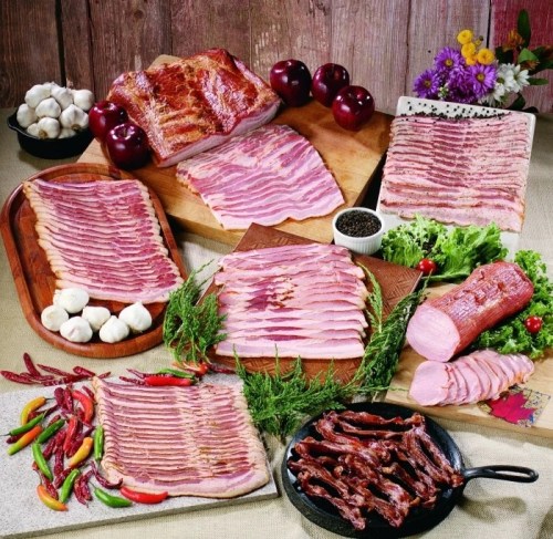 An assortment of cured meats, including bacon and ham, arranged with vegetables and garnishes on wooden and stone platters.