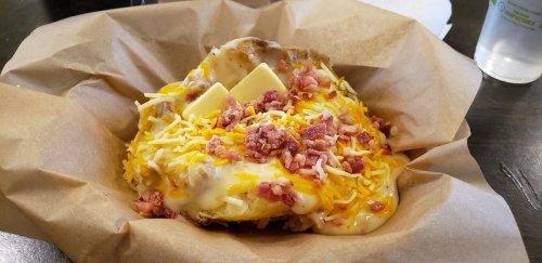 A baked potato topped with melted cheese, bacon bits, and butter, served in a paper-lined basket.