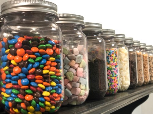 A row of glass jars filled with colorful candies and treats, neatly arranged on a shelf.