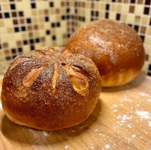 Two round loaves of freshly baked bread on a wooden surface, with a textured crust and a sprinkle of flour.