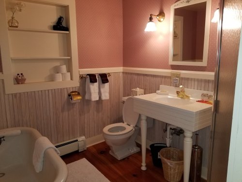 Cozy bathroom with a vintage tub, toilet, sink, and decorative wallpaper in soft colors.