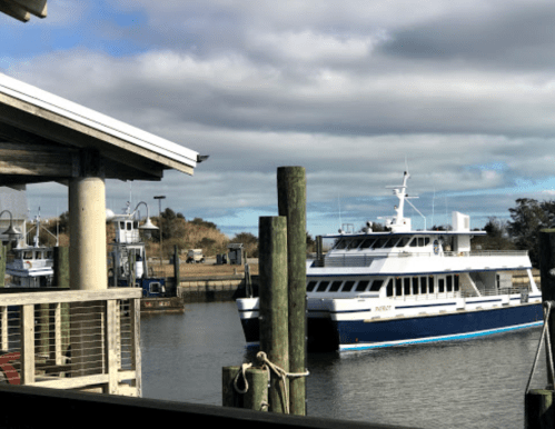 A ferry boat docked at a marina, with cloudy skies and wooden posts in the foreground.