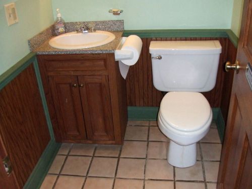 A small bathroom featuring a sink with a countertop, a toilet, and wooden paneling on the walls.