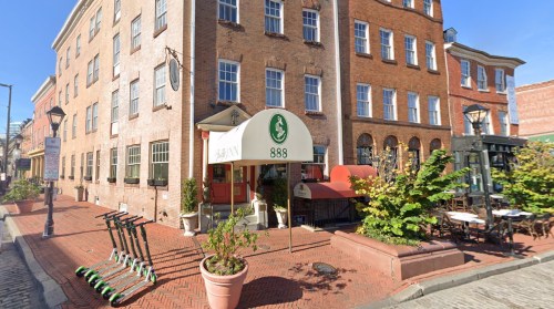 A brick building with a green awning labeled "888," outdoor seating, and scooters parked nearby on a sunny day.