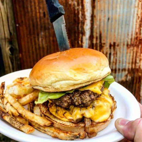 A juicy cheeseburger with lettuce and a knife on top, served with crispy fries on a white plate.