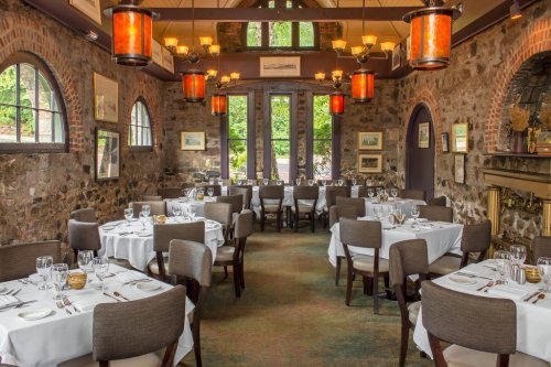 Elegant dining room with stone walls, white tablecloths, and warm lighting from hanging lanterns.