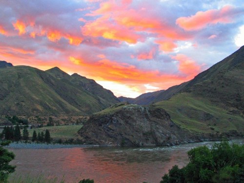 A vibrant sunset over mountains and a river, with colorful clouds reflecting in the sky.