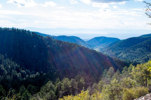 A scenic view of lush green mountains and valleys under a bright sky with rays of sunlight shining through.