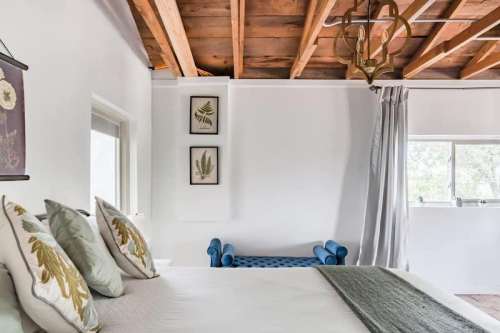 Bright bedroom with a wooden ceiling, decorative pillows, and a blue bench by the window. Minimalist decor.