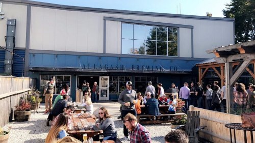 A bustling brewery with outdoor seating, people enjoying drinks, and a sunny day.