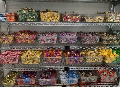 A colorful display of assorted candies in clear containers on metal shelves, organized by type and color.