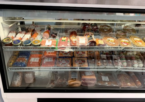 A refrigerated display case filled with various packaged meats, cheeses, and deli products.