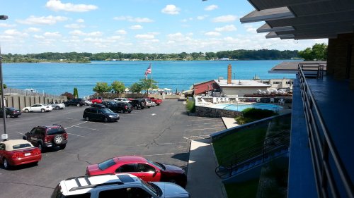 View of a parking lot with cars, a pool area, and a lake in the background under a clear blue sky.