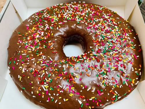 A large chocolate frosted donut topped with colorful sprinkles, placed in a white box.