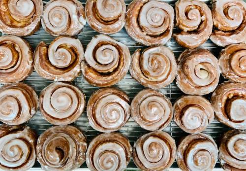 A close-up of freshly baked cinnamon rolls with a glossy icing, arranged neatly on a cooling rack.