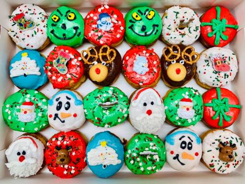 A festive assortment of decorated donuts featuring Christmas themes like Santa, snowmen, and reindeer in a box.