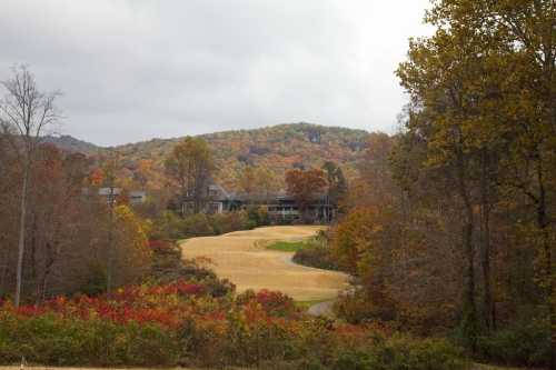 A scenic view of a golf course surrounded by autumn foliage and rolling hills under a cloudy sky.