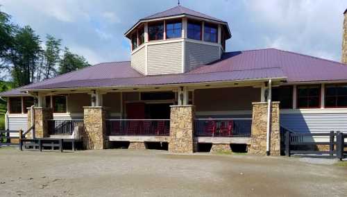 A modern building with a stone facade and a purple roof, featuring large windows and a porch with red chairs.