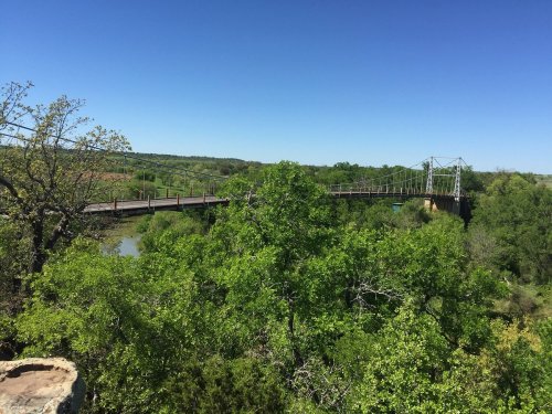 A scenic view of a bridge over a river, surrounded by lush green trees and a clear blue sky.