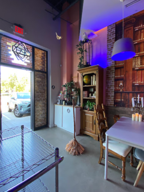 Cozy café interior with bookshelves, a broom, and a welcoming entrance, featuring warm lighting and rustic decor.