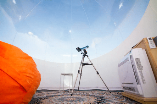 A cozy observatory with a telescope, a bean bag, and an air conditioner, under a clear sky.